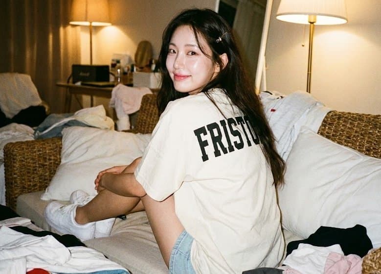 A woman sits with her back to the audience on a woven sofa.